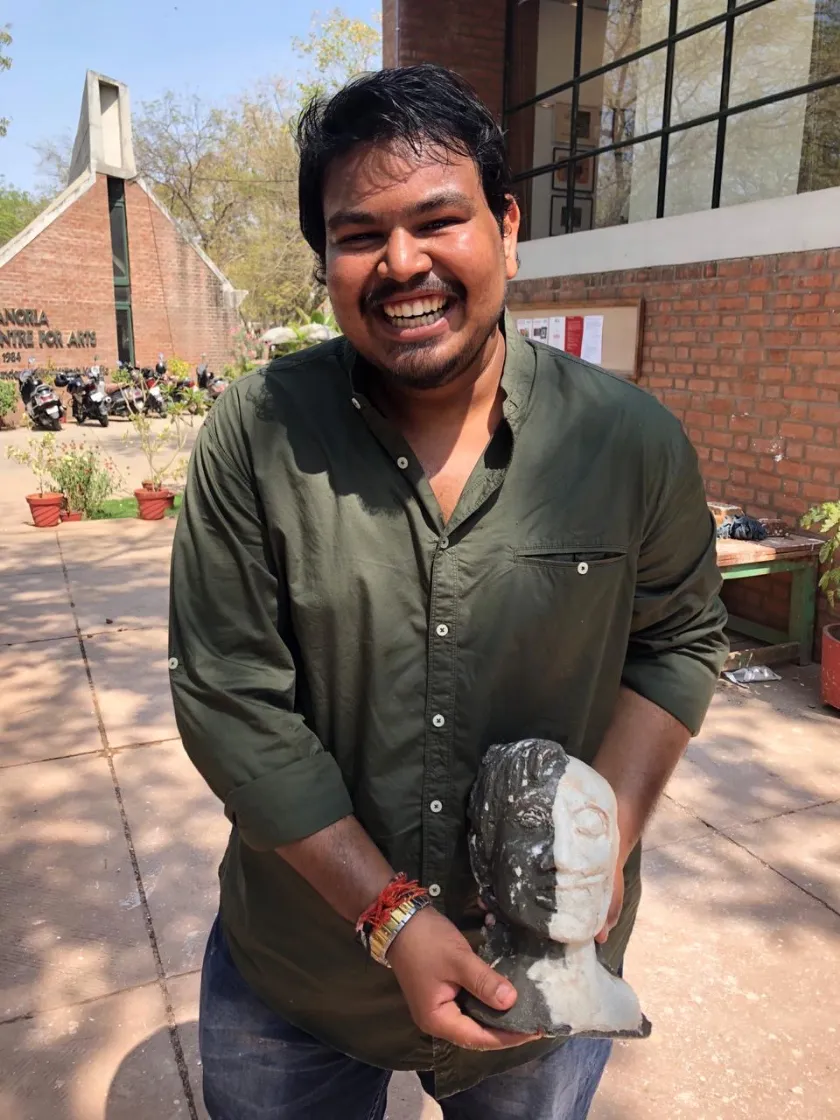 Sourabh Kori smiling outside an arts centre, holding a half-dark, half-white stone head meant to be Harvey Dent.